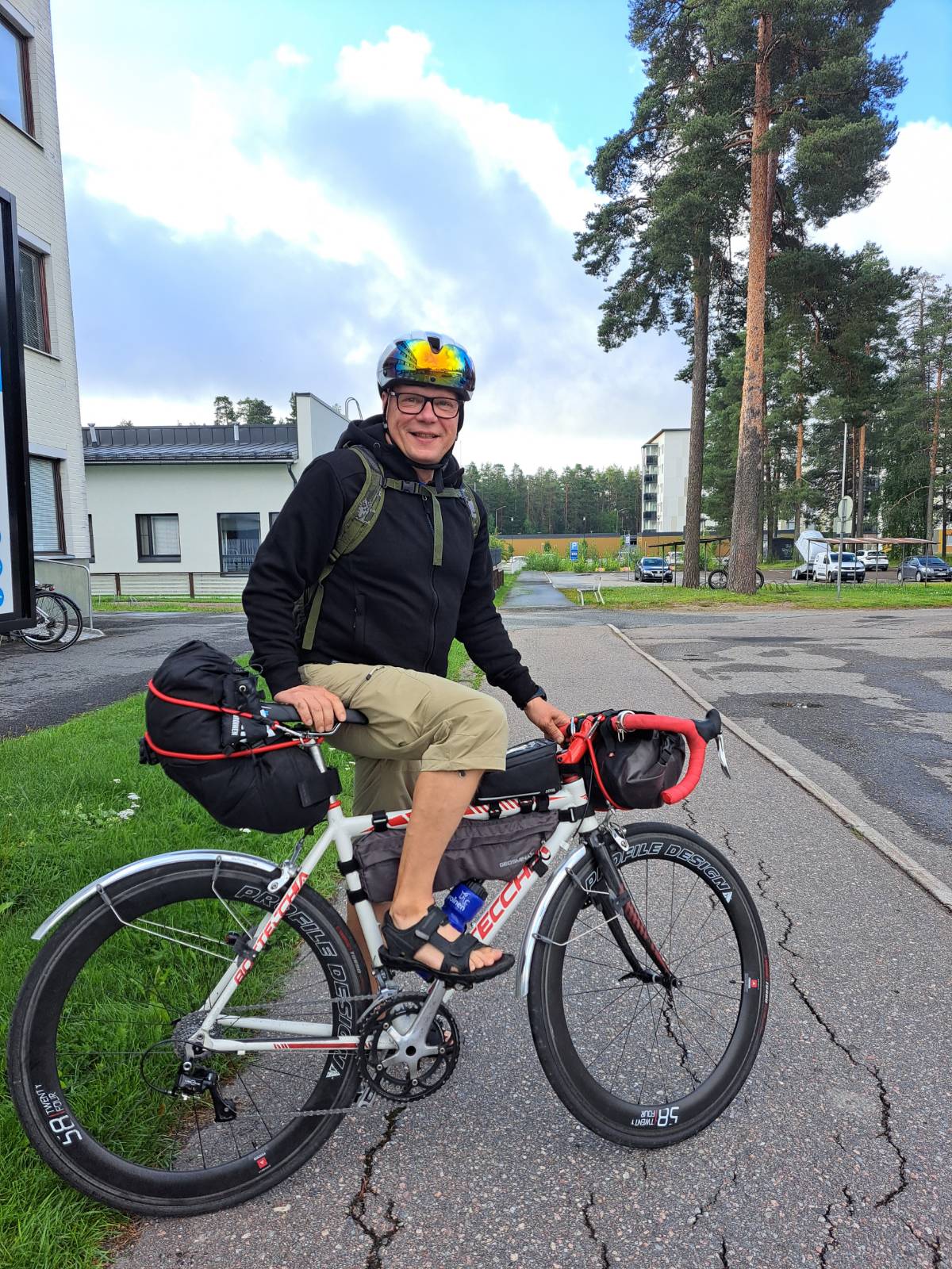 Tässä on kuva Jormasta, joka seisoo polkupyörän kanssa ja katsoo hymyillen kameraan
